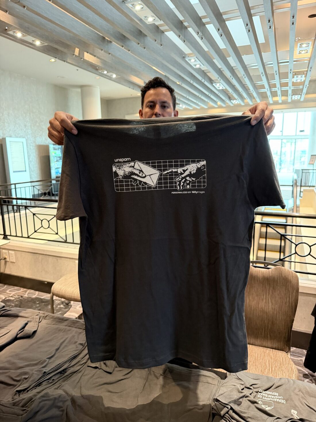 Guest holding up a freshly printed black tee with a custom two-hands graphic in a hotel lobby