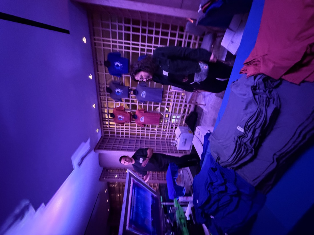 Pop-up customization shop with display shirts on a lattice wall and staff preparing equipment at an evening conference