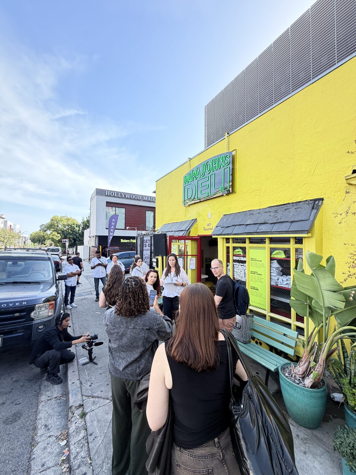 Crowd gathered outside a bright yellow popup storefront hosting a hat and merch customization bar during an LA street fair