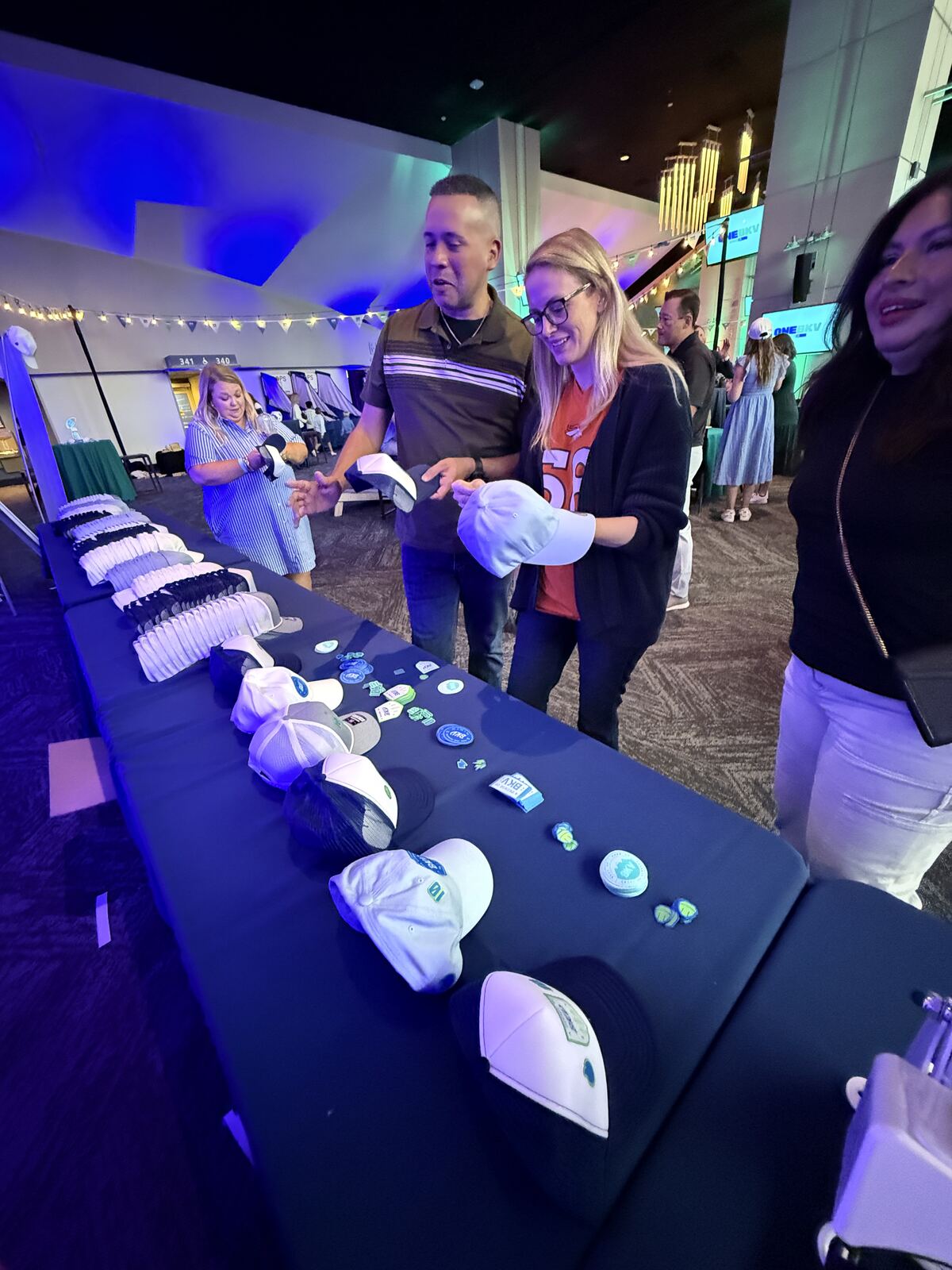 Two guests comparing trucker hats over a long patch selection table at an indoor corporate event